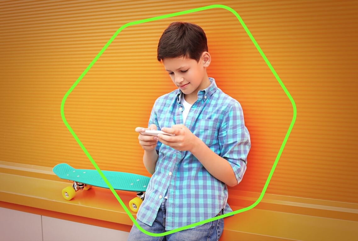 çocuk elinde telefon ile duvara yaslanmış oyun oynuyor.